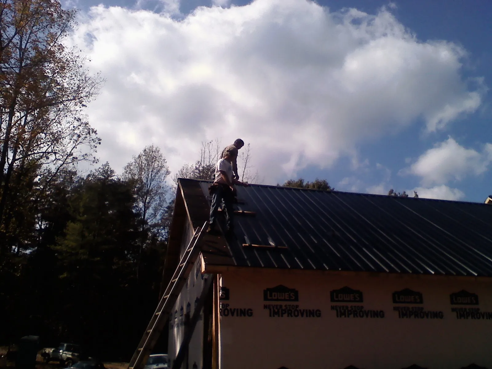 Roofer fastening dark metal panels high against a cloudy sky, from a Roof Inspection job in Mc Donald