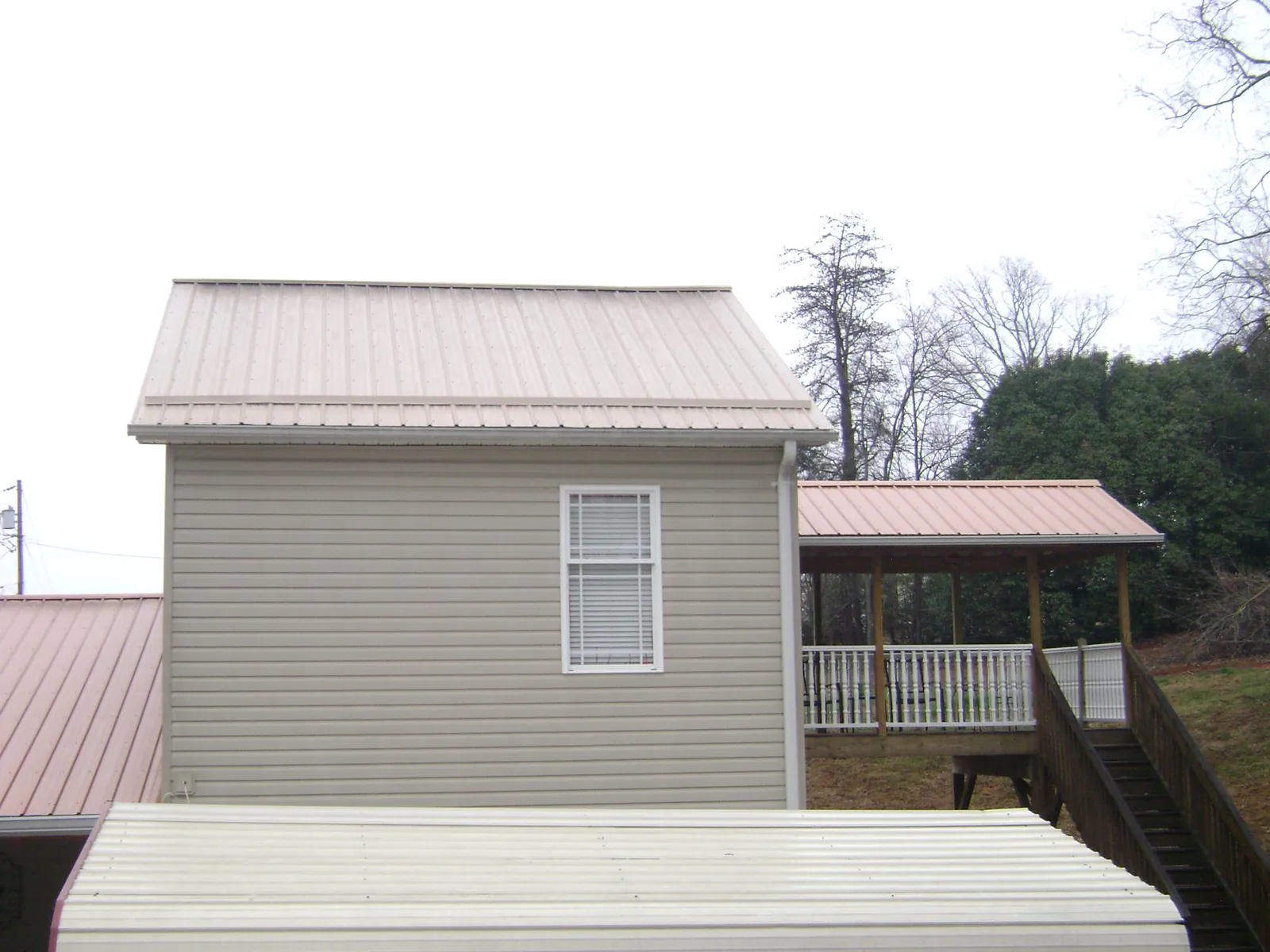 Tan metal roofs on a two story addition and attached porch, from a Roof Replacement job in Mc Donald